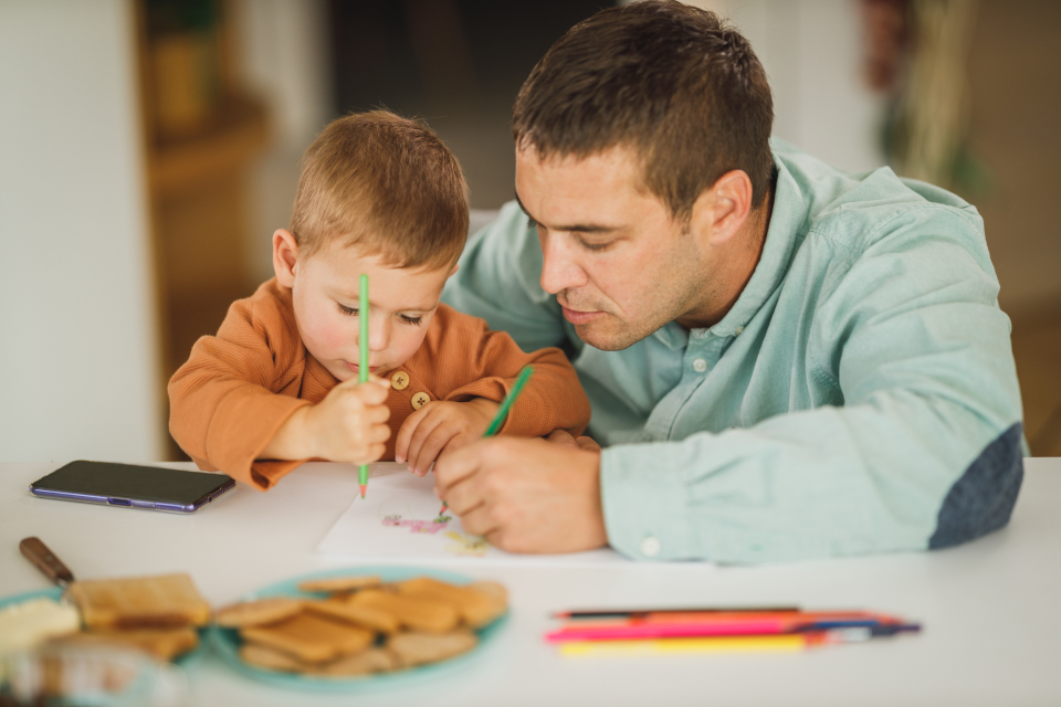 A father and his young son drawing together at a table